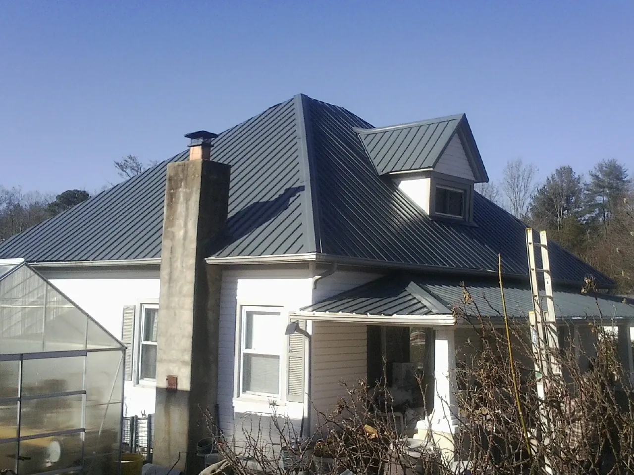Dark blue standing seam metal roof on a white farmhouse with dormer — Slate & Tile Roof Repair by Roofing Brothers in Semora
