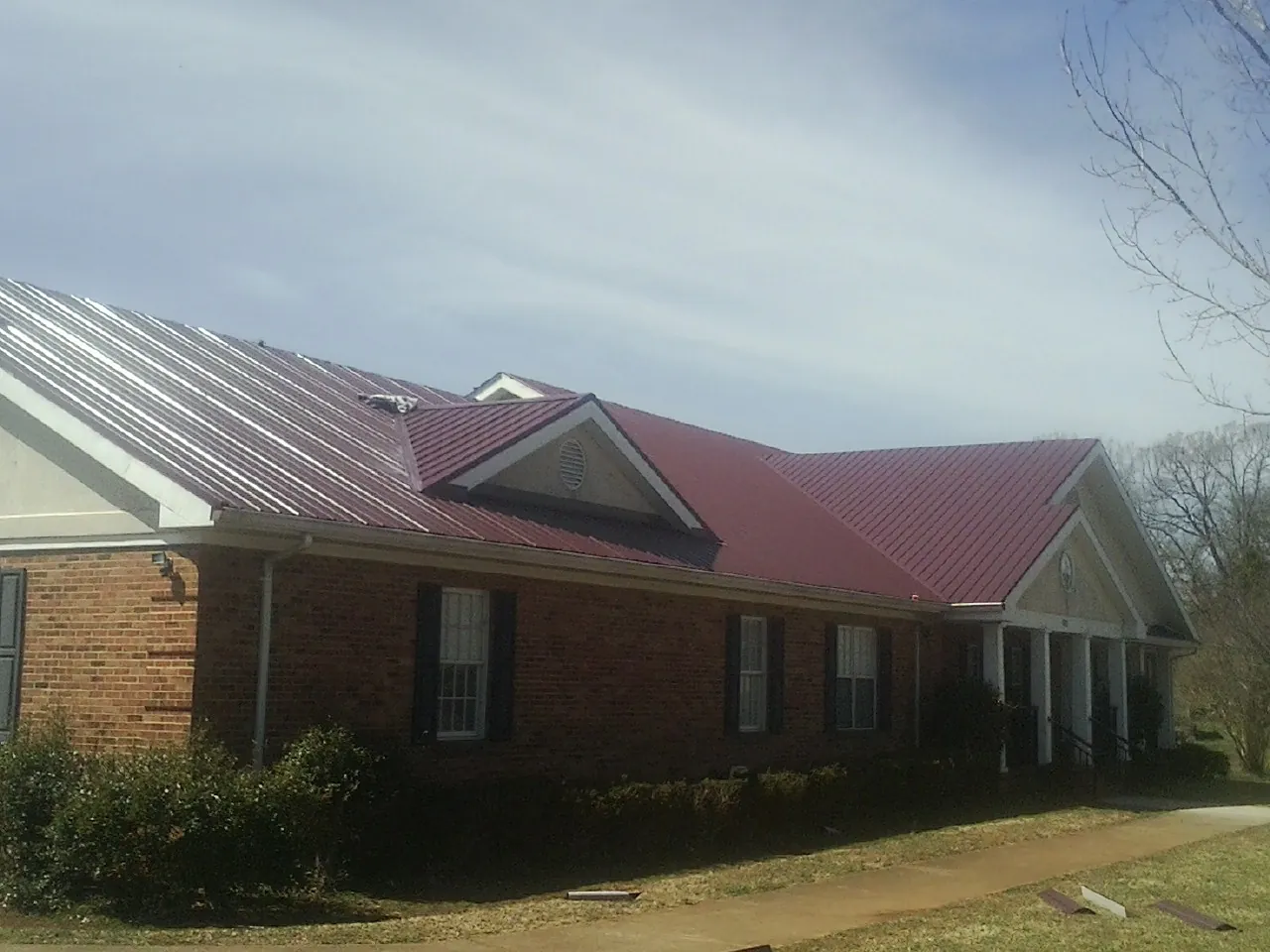 Red metal roof with gabled entries on a long brick building, from a Hail Damage Roof Repair job in Semora
