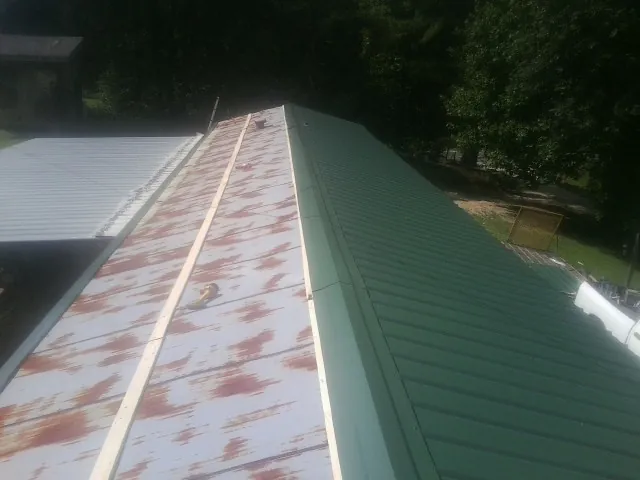 Old rusted panels beside newly installed green metal roofing — Wind Damage Roof Repair by Roofing Brothers in Semora