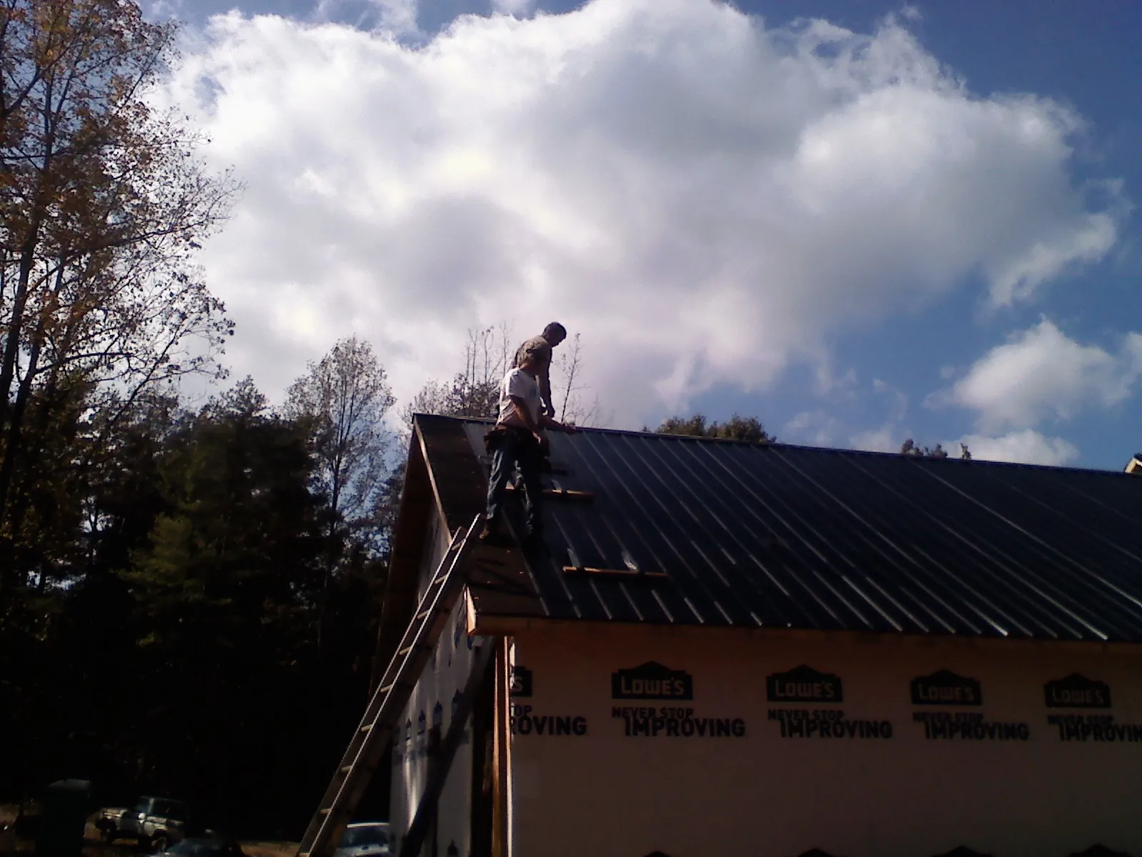 Roofer fastening dark metal panels high against a cloudy sky, from a Roof Inspection job in Semora
